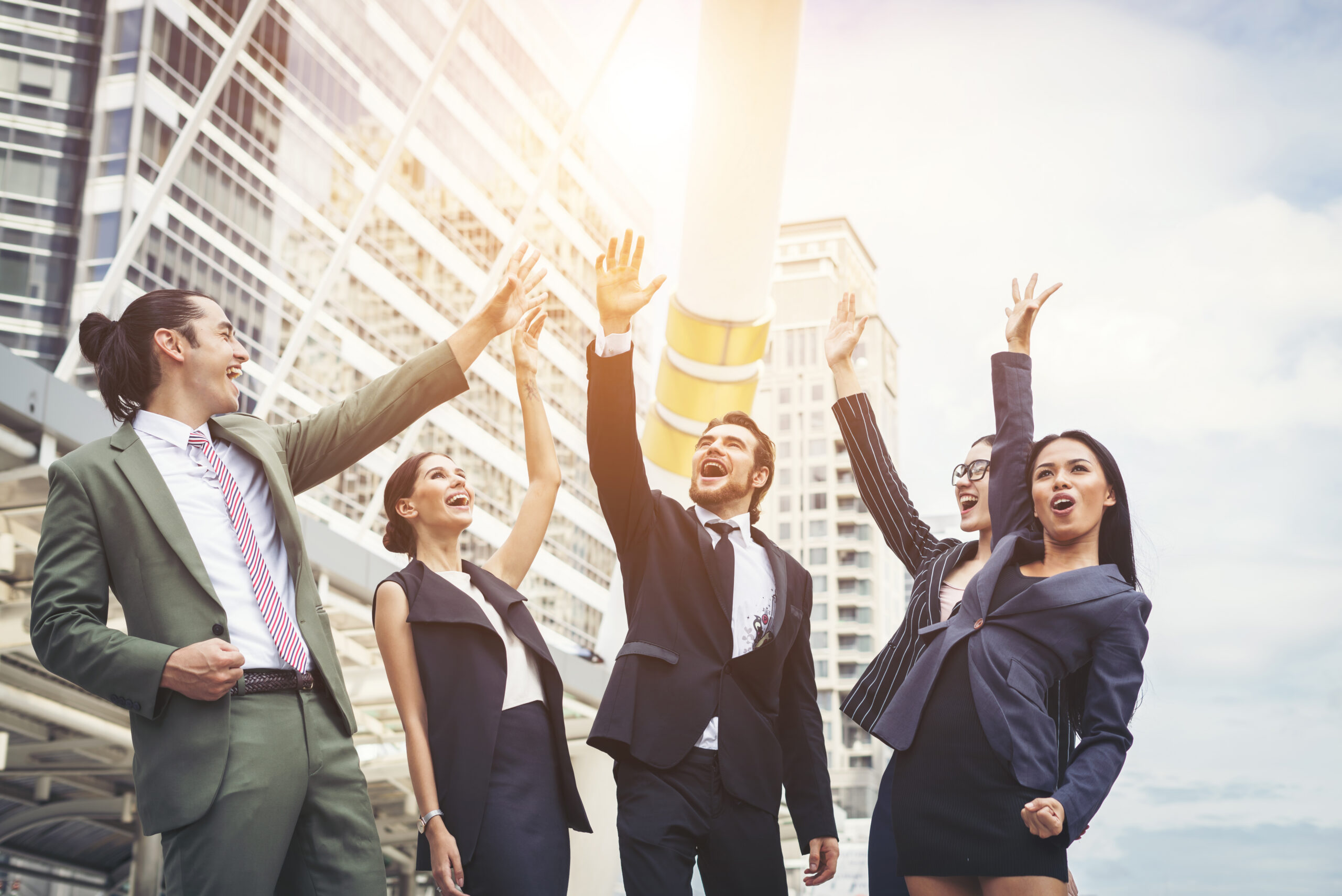 A group of five happy colleagues have their hands up in the air, illustrating career growth.